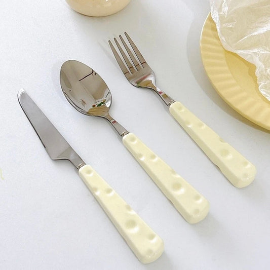 Set of silver cutlery with cream-colored handles on a white surface.