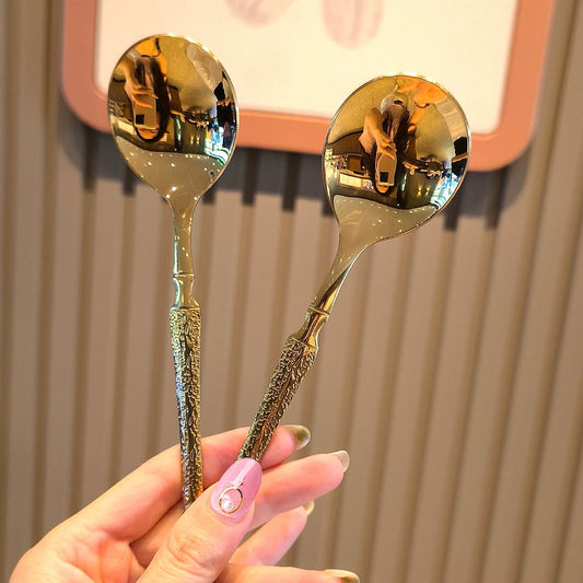 Two ornate silver spoons held by a hand with pink nail polish against a neutral background.