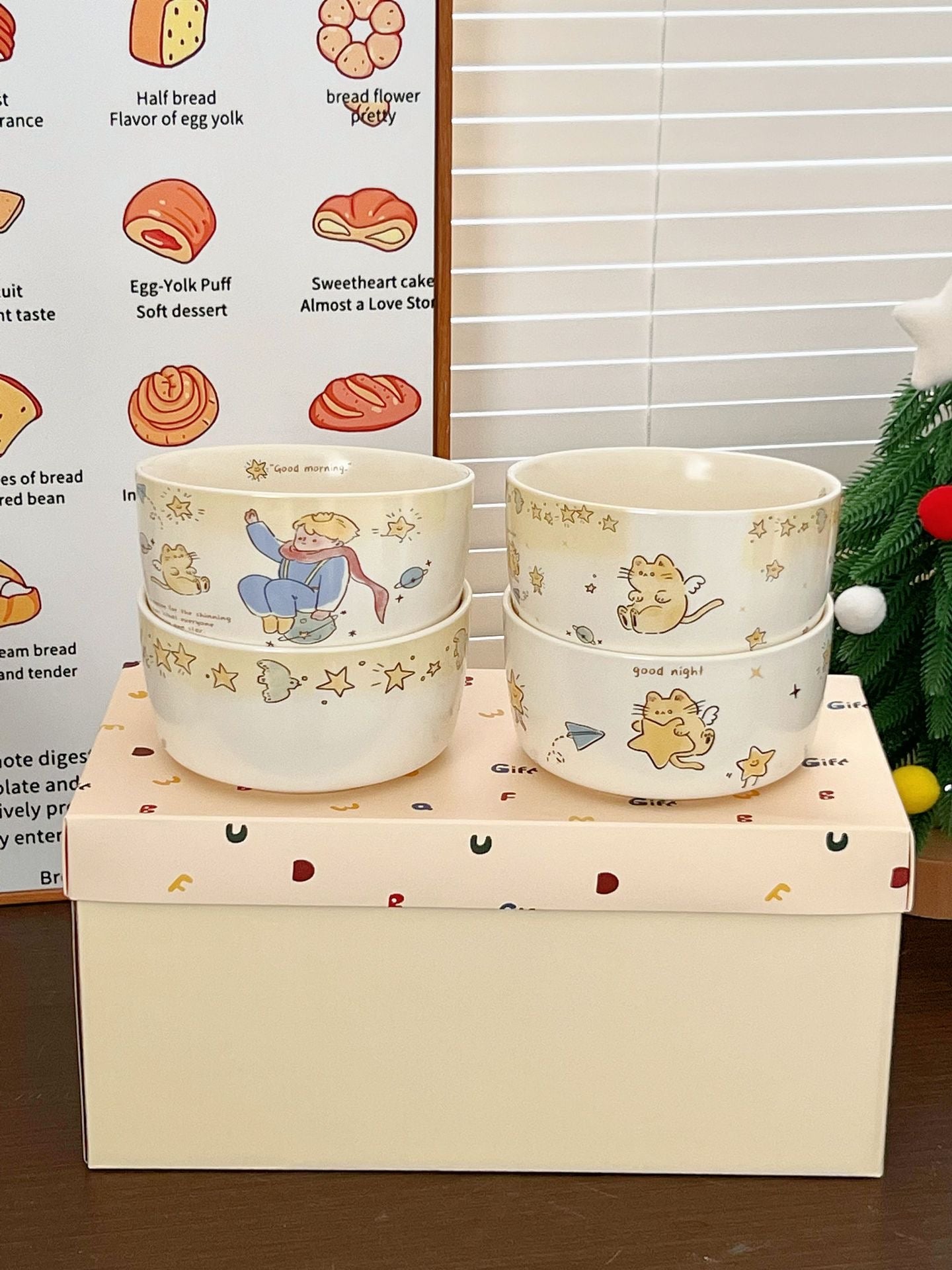 Two stacked ceramic bowls with cartoon designs on a box with a Christmas tree in the background.