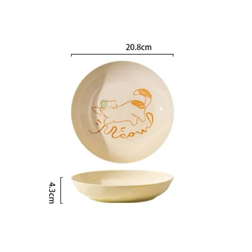 Ceramic bowl and plate set with playful cat illustrations, displayed with food and kitchen accessories.