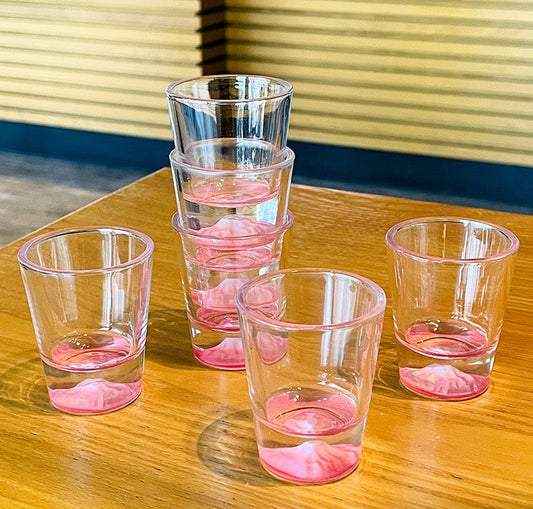 A set of clear shot glasses with pink lip imprints at the bottom, arranged on a wooden table.