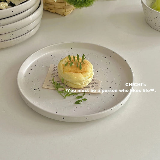 Minimalist speckled ceramic plate on a white table with a modern black-and-white striped fork.