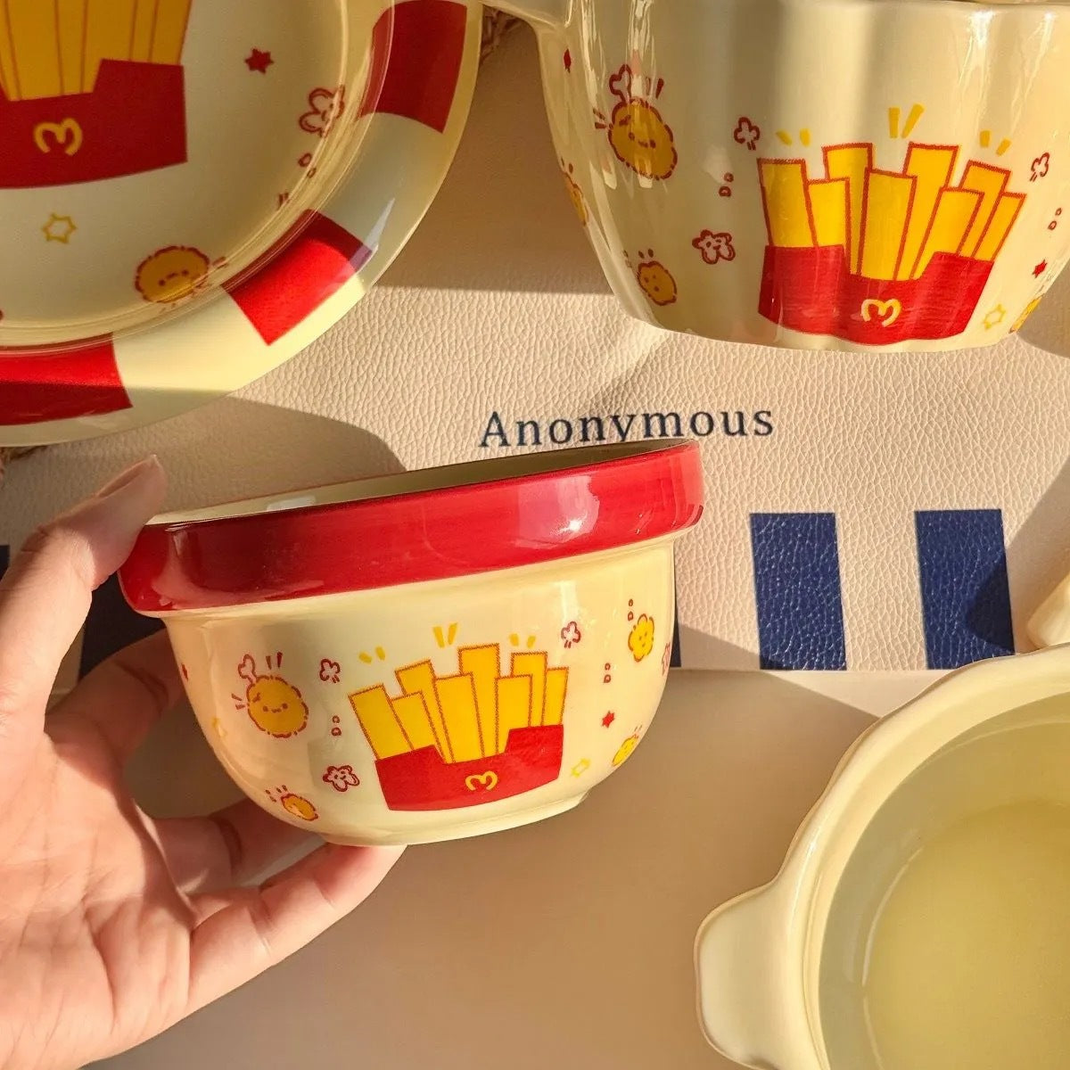 Child's bowl with French fries design held by a hand, with other bowls in the background.