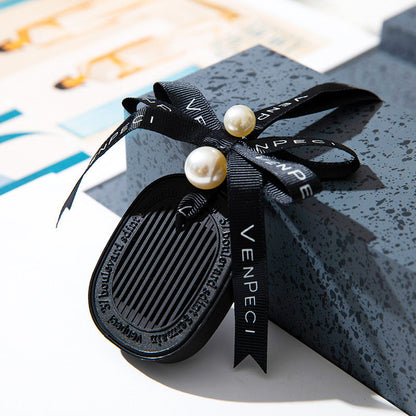 Elegant black car air freshener with pearl and ribbon, attached to a gift box.