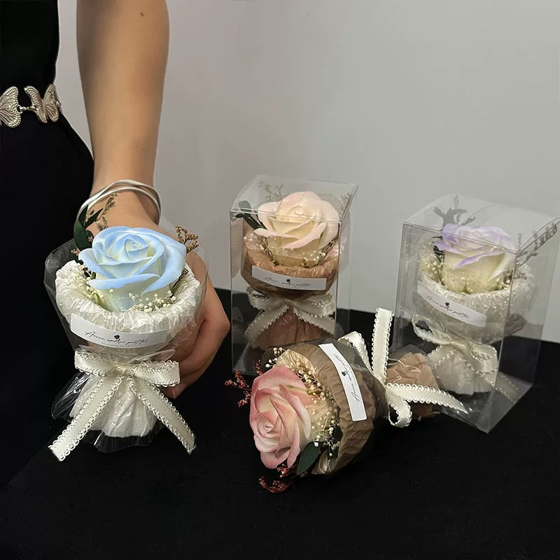 A collection of mini pocket rose bouquets in different pastel colors, elegantly wrapped with lace and ribbons, displayed in clear packaging and held in hand.