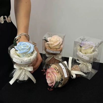 A collection of mini pocket rose bouquets in different pastel colors, elegantly wrapped with lace and ribbons, displayed in clear packaging and held in hand.