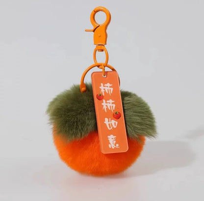 A hand holding a persimmon-colored keychain with a plush texture and a tag with Chinese characters on it.
