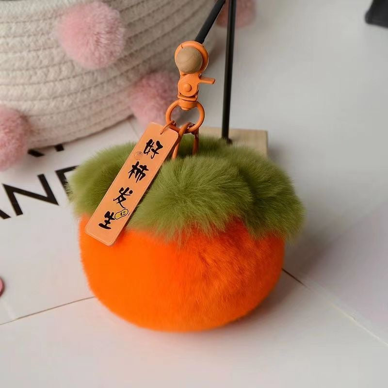 A hand holding a persimmon-colored keychain with a plush texture and a tag with Chinese characters on it.