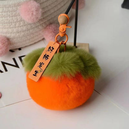 A hand holding a persimmon-colored keychain with a plush texture and a tag with Chinese characters on it.