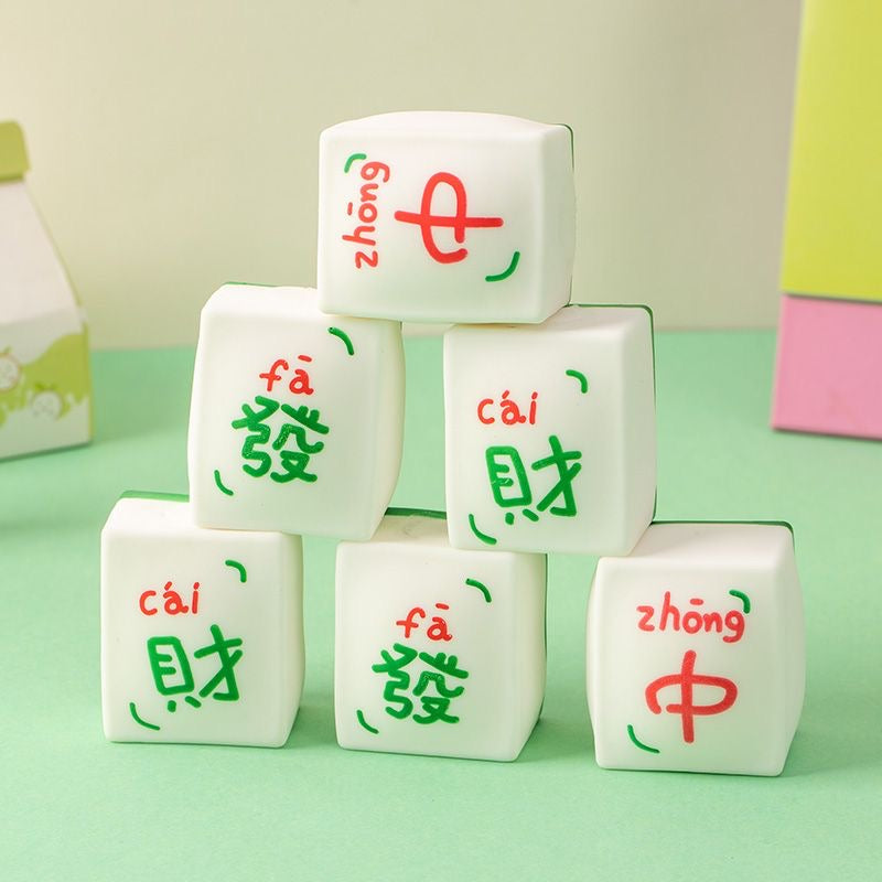 A hand pressing a Mahjong Squishy Toy, showcasing its soft and flexible texture, with multiple Mahjong-styled squishy tiles in the background.