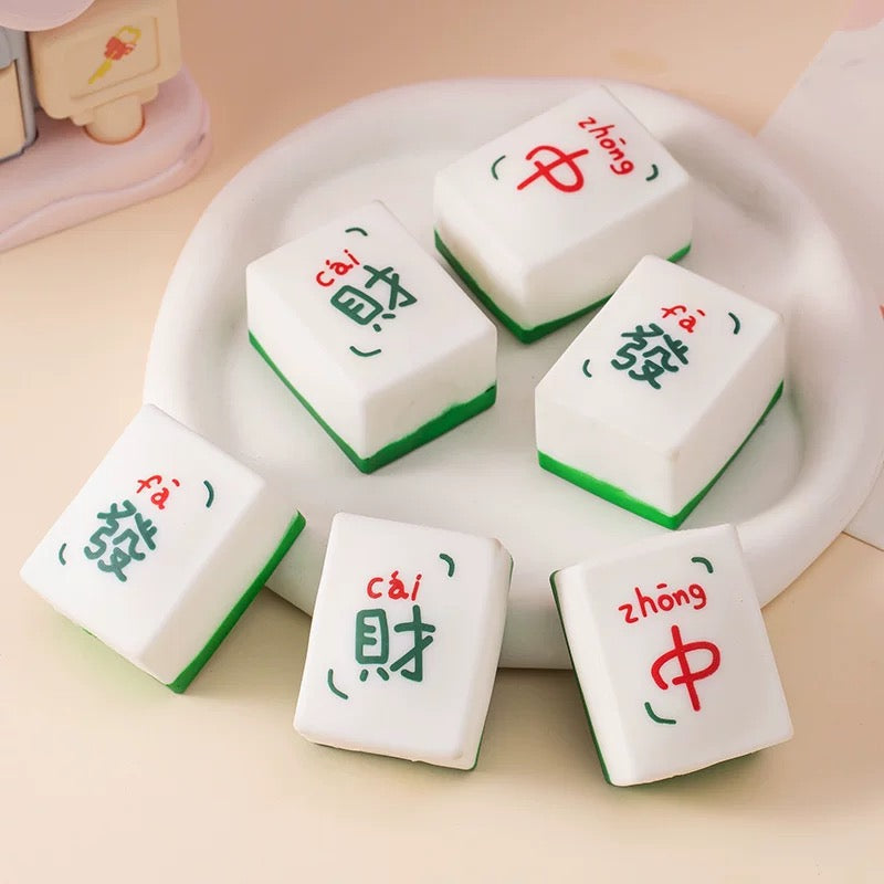 A collection of white squishy mahjong tiles with red and green Chinese characters on them, arranged in a stack on a green background.