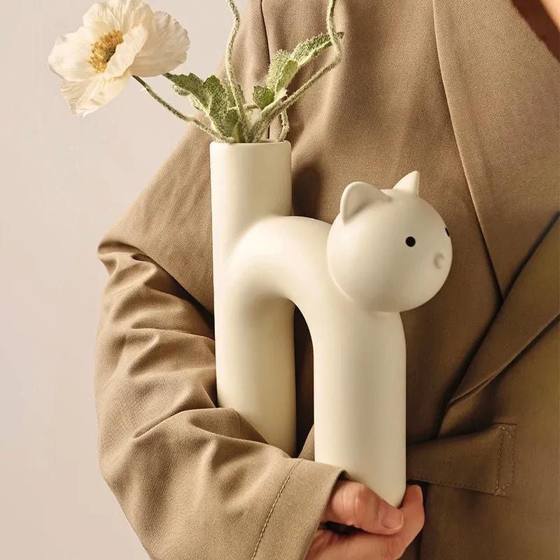 Person holding a white cat-shaped vase with flowers against a beige background