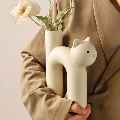 Person holding a white cat-shaped vase with flowers against a beige background