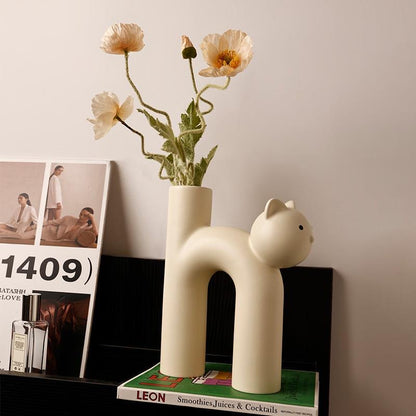 Cat-shaped vase with flowers on a shelf next to a magazine