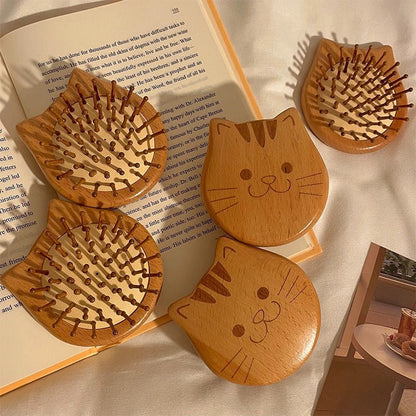 Wooden cat-shaped hair brushes with engraved cat faces, placed on a book and soft fabric background.