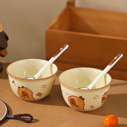 Two ceramic bowls with cartoon bear designs and white spoons on a wooden surface.