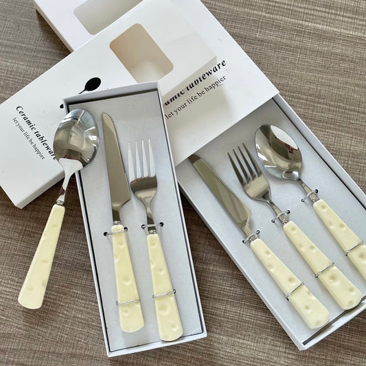 Set of silverware with cream-colored handles in a box on a textured surface