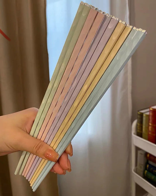 A hand holding pastel-colored diamond-tipped chopsticks with a luxurious design.