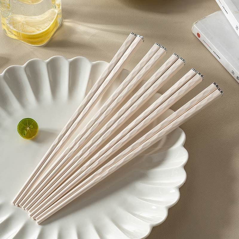 A pair of sleek, pastel-toned chopsticks with hammered texture and diamond-inspired tips, displayed on a white plate.