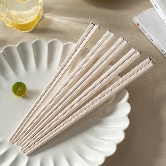 A pair of sleek, pastel-toned chopsticks with hammered texture and diamond-inspired tips, displayed on a white plate.