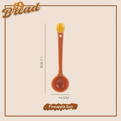 A set of ceramic measuring spoons with cute snack-themed handles, displayed in a kitchen setting.