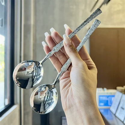Hand holding three silver spoons with intricate designs against a blurred indoor background