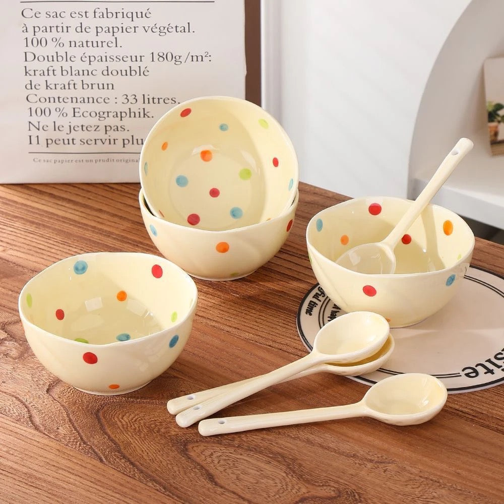 A set of ceramic bowls with colorful polka dots on a wooden surface, accompanied by matching ceramic spoons.