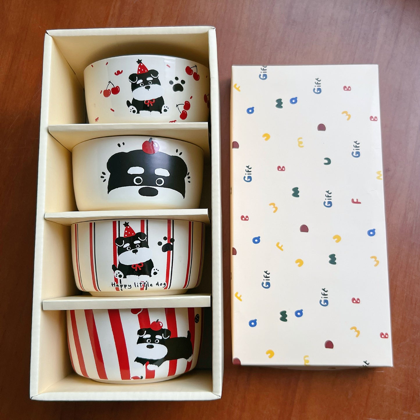 Set of four ceramic bowls with dog illustrations in a box, next to a colorful patterned box.