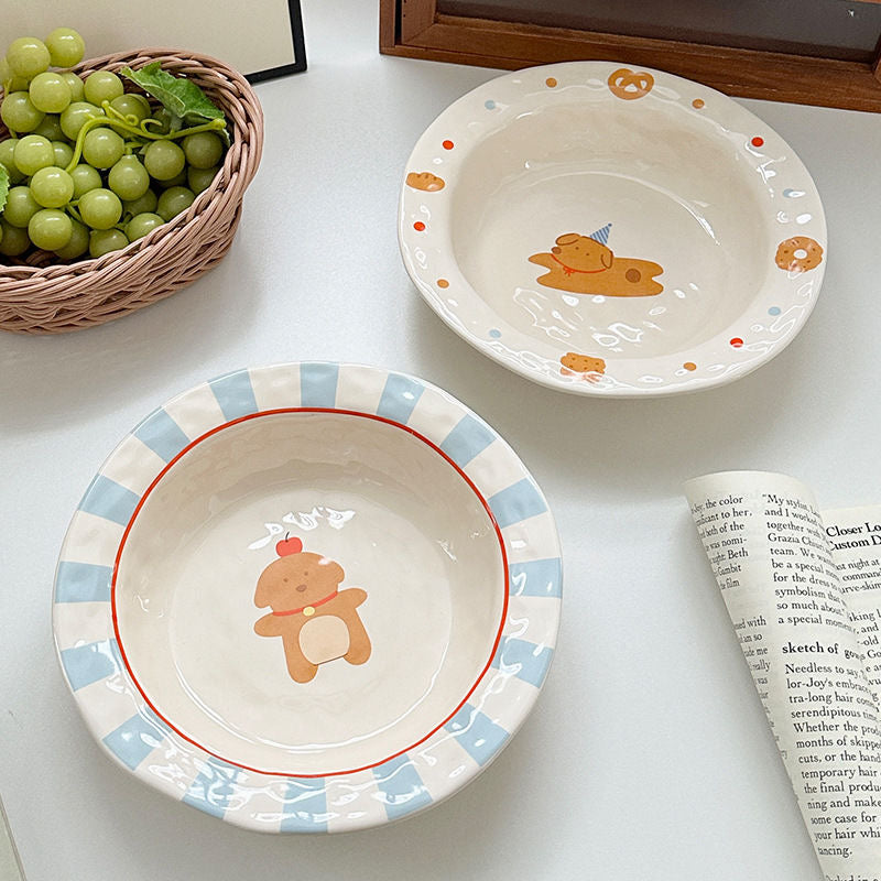 Two ceramic bowls with teddy bear designs on a white surface with grapes and a book.