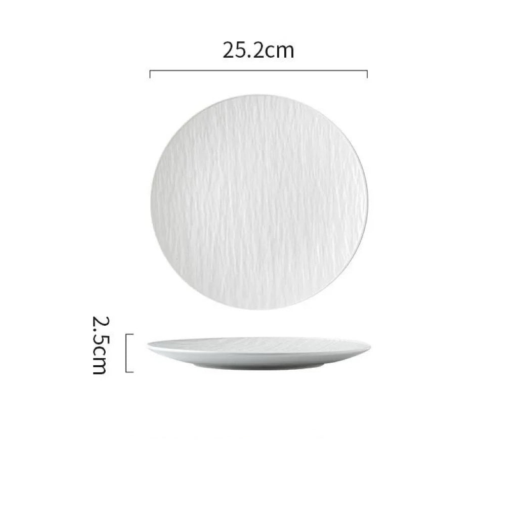 A black textured dinner plate with a matte finish, displayed on a gray surface with a napkin, wooden pepper grinder, and cutlery set to the side. A piece of food is served on the plate, showcasing its use in a dining setting.