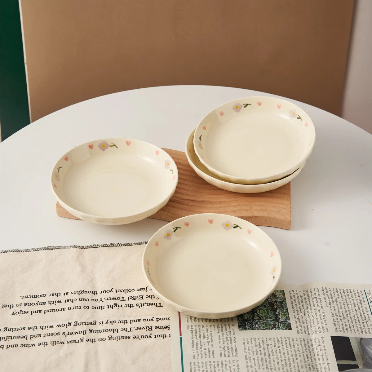 Hand-painted ceramic plates with heart and flower designs neatly stacked in a wooden dish rack, with floral artwork and a cozy table setting in the background.