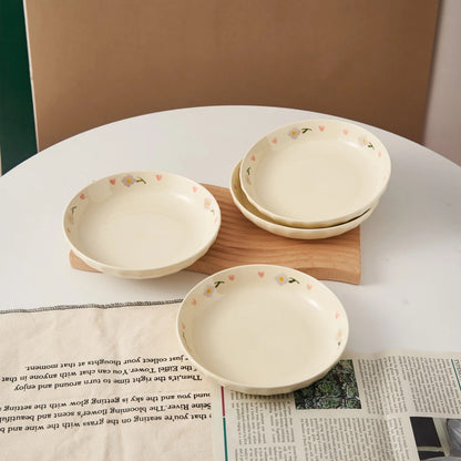 Hand-painted ceramic plates with heart and flower designs neatly stacked in a wooden dish rack, with floral artwork and a cozy table setting in the background.