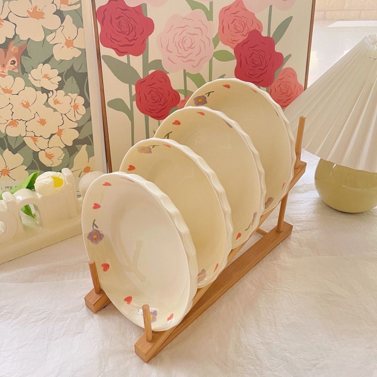 A set of hand-painted ceramic plates with a wisteria flower design, displayed on a wooden plate stand, with floral wallpaper in the background.
