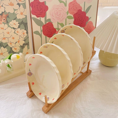 A set of hand-painted ceramic plates with a wisteria flower design, displayed on a wooden plate stand, with floral wallpaper in the background.