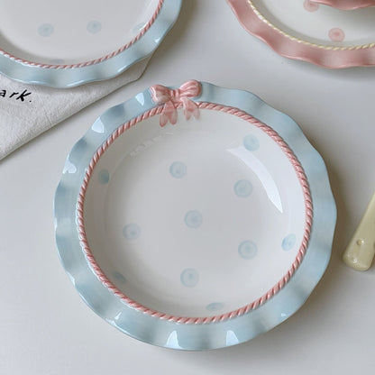 A set of ceramic tableware with a polka dot pattern and bow-knot detail, displayed in blue and pink colors.