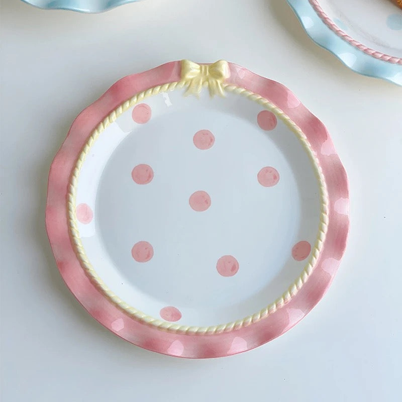 A set of ceramic tableware with a polka dot pattern and bow-knot detail, displayed in blue and pink colors.
