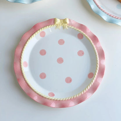 A set of ceramic tableware with a polka dot pattern and bow-knot detail, displayed in blue and pink colors.