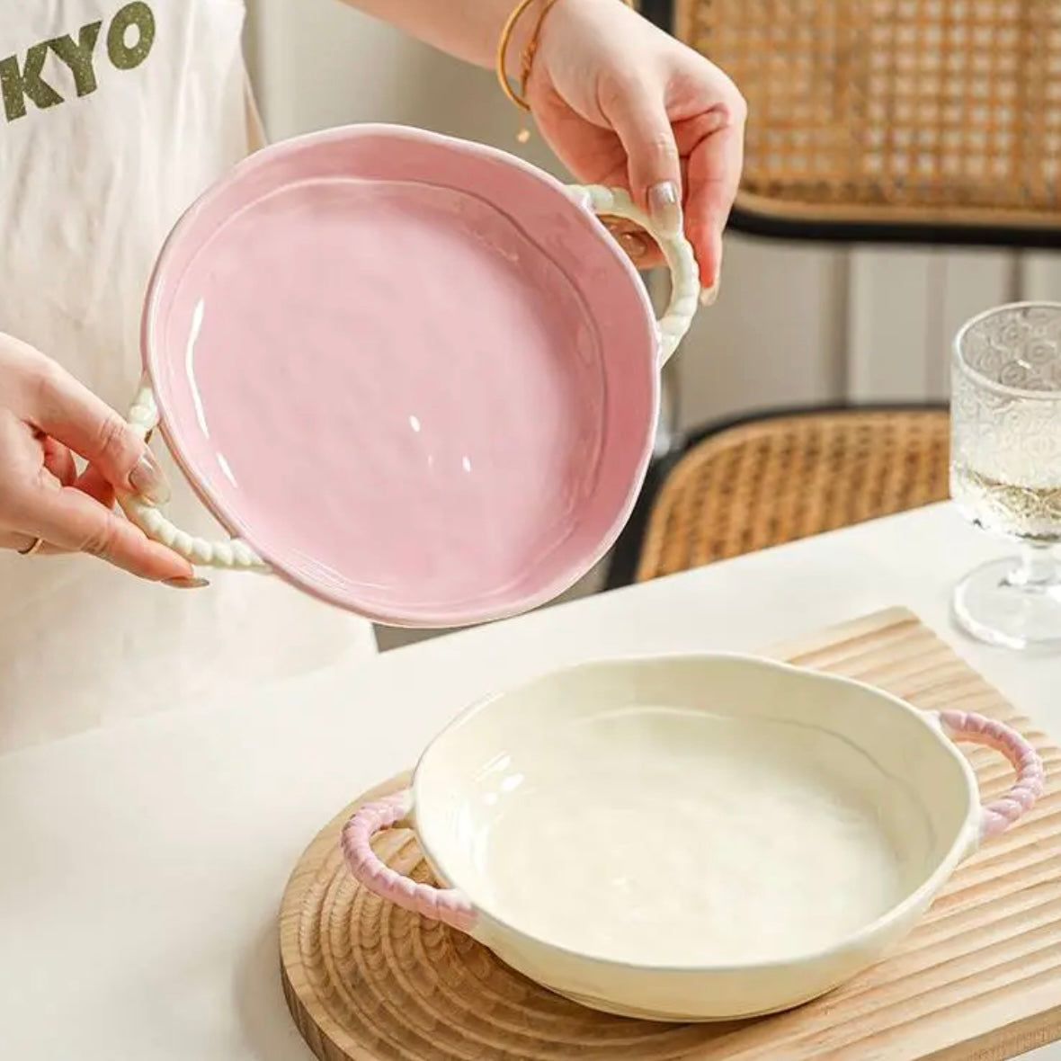Person holding a pink ceramic dish with another dish on a table.