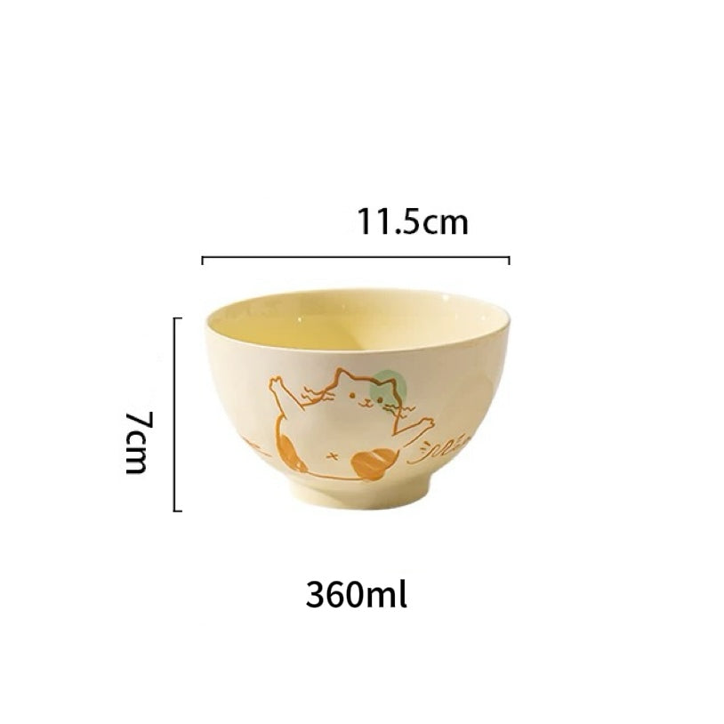 Ceramic bowl and plate set with playful cat illustrations, displayed with food and kitchen accessories.