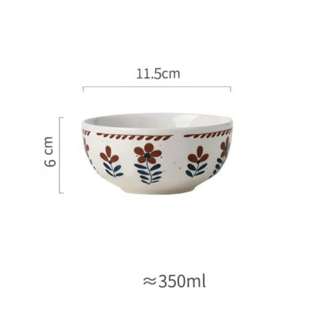 A ceramic bowl with hand-painted floral designs in warm earthy tones on a white background, alongside parts of other bowls and plates.