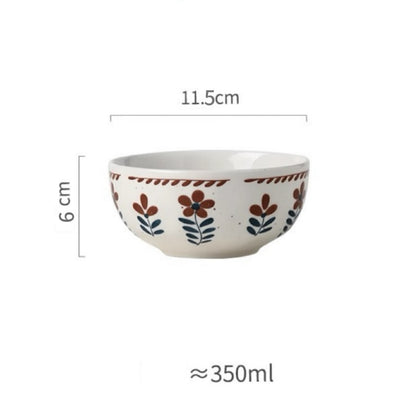 A ceramic bowl with hand-painted floral designs in warm earthy tones on a white background, alongside parts of other bowls and plates.