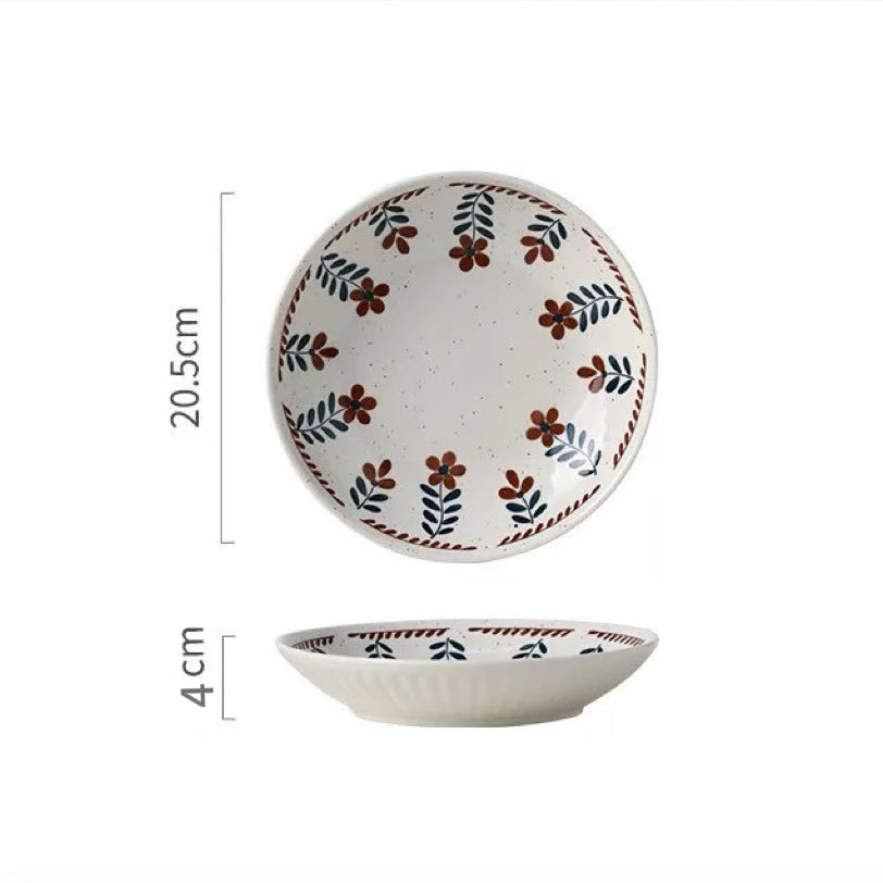 A ceramic bowl with hand-painted floral designs in warm earthy tones on a white background, alongside parts of other bowls and plates.
