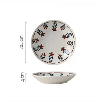 A ceramic bowl with hand-painted floral designs in warm earthy tones on a white background, alongside parts of other bowls and plates.