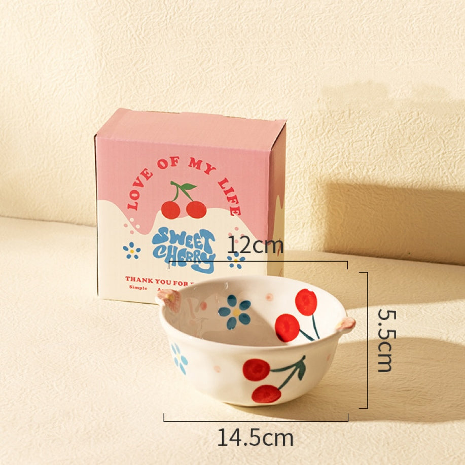 Ceramic bowl with cherry design next to its packaging on a beige surface