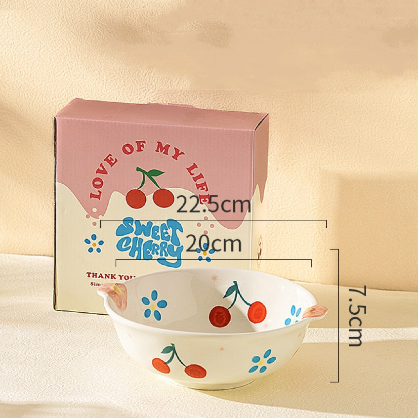 Ceramic bowl with cherry design next to its packaging on a beige background