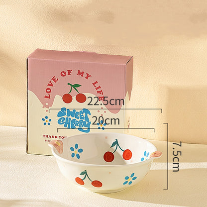 Ceramic bowl with cherry design next to its packaging on a beige background
