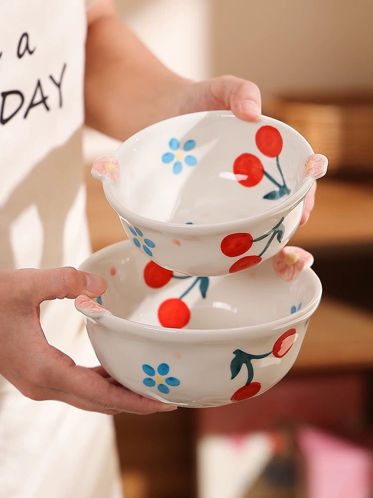 Two stacked ceramic bowls with cherry and flower designs held by a person.
