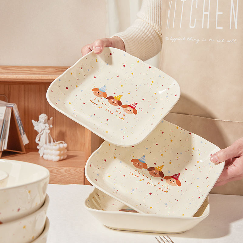 Person holding a set of ceramic trays with cartoon designs in a kitchen setting.
