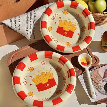 Two children's plates with red and white design featuring cartoon fries, a spoon, and a basket of apples on a wooden surface.