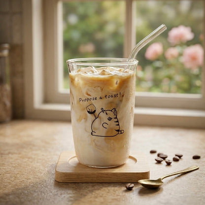 Glass of iced coffee with a straw on a wooden coaster, surrounded by coffee beans and a spoon, with a blurred outdoor background.